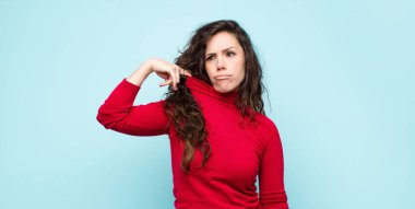 Genç, güzel bir kadın stresli, endişeli, yorgun ve hayal kırıklığına uğramış, gömleğini çekmiş, mavi duvara karşı sorunlu görünüyor.