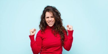 Genç, güzel bir kadın mutlu, pozitif ve başarılı hissediyor, zaferi kutluyor, başarıları kutluyor ya da mavi duvara karşı iyi şanslar diliyor.