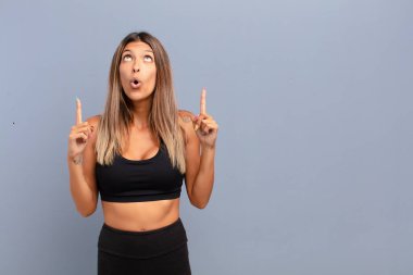 Genç ve güzel bir kadın huşu içinde ve ağzı açık bir şekilde şaşkın ve şaşkın bir bakışla yukarıya bakıyor.