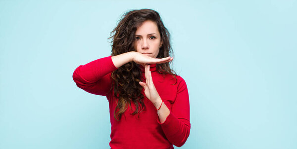 молодая красивая женщина выглядит серьезным, строгим, сердитым и недовольным, делая время знак против синей стены