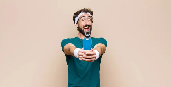 young sports man with an energy drink bottle against flat wall