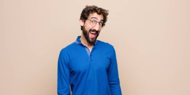 Genç, yakışıklı, büyük, dost canlısı, kaygısız bir gülümsemesi olan, pozitif görünen, rahat ve mutlu görünen, düz duvara karşı ürperen bir adam.