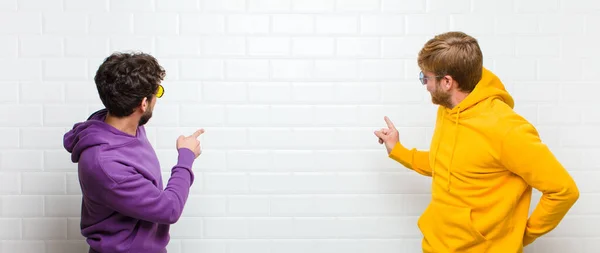 若いクールな男性が立ってコピースペースにオブジェクトを指して 白いタイルの壁に対するリアビュー — ストック写真