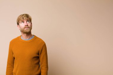 Endişeli, kafası karışık, budala bir ifadeyle genç sarışın adam kopya alanı arıyor, düz duvara karşı şüpheyle bakıyor.