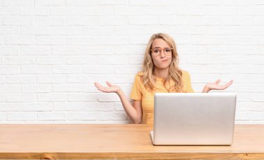 Genç sarışın kadın şaşkın ve şaşkın hissediyor, şüpheci, farklı seçenekleri tartıyor ya da seçiyor. Komik bir ifadeyle dizüstü bilgisayar kullanıyor.
