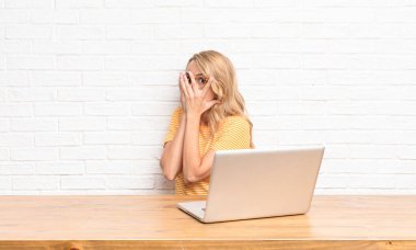 Genç, sarışın bir kadın korkmuş ya da utanmış hissediyor. Gözleri yarı kapalı, dizüstü bilgisayar kullanarak dikizliyor ya da dikizliyor.