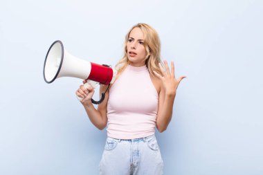 Genç, sarışın bir kadın stresli, endişeli, yorgun ve hayal kırıklığına uğramış, gömleğini çekmiş, megafonla ilgili sıkıntıları olan biri gibi görünüyor.