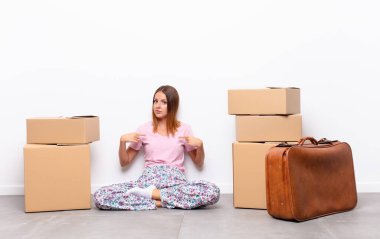 kızıl saçlı güzel bir kadın gururlu, pozitif ve rahat görünüyor. Yeni bir evde iki eliyle göğsünü gösteriyor.