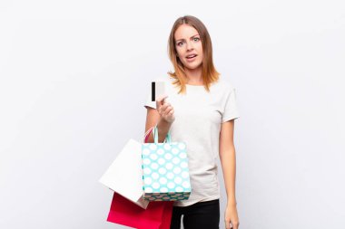 red head pretty woman feeling puzzled and confused, with a dumb, stunned expression looking at something unexpected with shopping bags