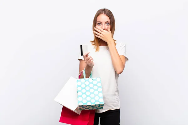 赤い頭の可愛い女が手で口を覆いショッピングバッグで秘密を守るか口を開く — ストック写真