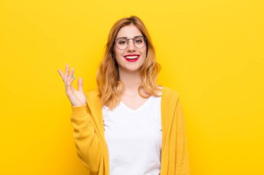 Genç, güzel sarışın kadın mutlu, şaşırmış ve neşeli, pozitif bir tavırla gülümsüyor, sarı duvara karşı bir çözüm ya da fikir buluyor.