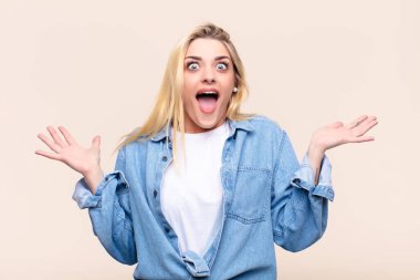 Genç, güzel sarışın kadın mutlu, heyecanlı, şaşırmış ya da şok olmuş hissediyor, gülümsüyor ve şaşırıyor.