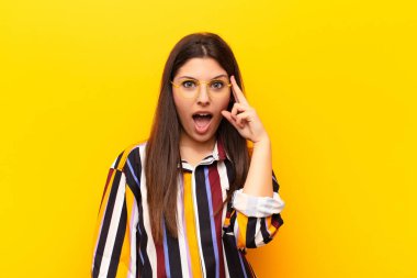 Genç, güzel bir kadın şaşırmış, ağzı açık, şok olmuş, sarı duvara karşı yeni bir düşünce, fikir ya da konsept keşfediyor.