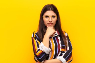Genç, güzel bir kadın ciddi görünüyor, kafası karışık, kararsız ve düşünceli, sarı duvara karşı seçenekler veya seçimler arasında şüpheci.