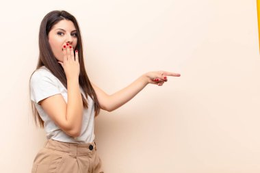 Genç, güzel bir kadın kendini mutlu, şok olmuş ve şaşırmış hissediyor. Ağzını eliyle kapatıyor ve yanal kopya alanını işaret ediyor.