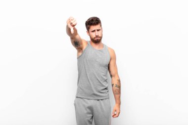 Huysuz, sinirli, sinirli, hayal kırıklığına uğramış ya da hoşnutsuz genç bir adam ciddi bir bakışla baş parmağını aşağı gösteriyor. spor konsepti