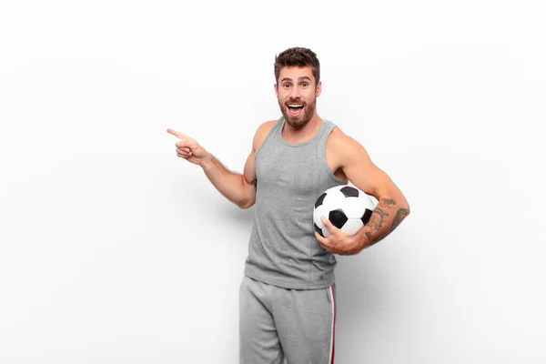 サッカーボールを持っているスペースをコピーするには 側と上を指して興奮して驚いている若いハンサムな男 — ストック写真