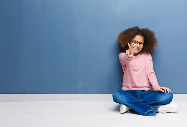 美国黑人小女孩面带微笑 看上去快乐 无忧无虑 积极向上 一只手坐在地板上表示胜利或和平 — 图库照片