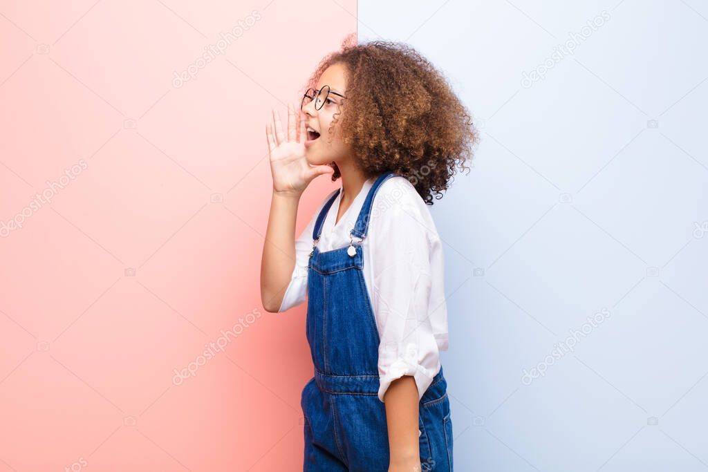 african american little girl profile view, looking happy and excited, shouting and calling to copy space on the side against flat wall