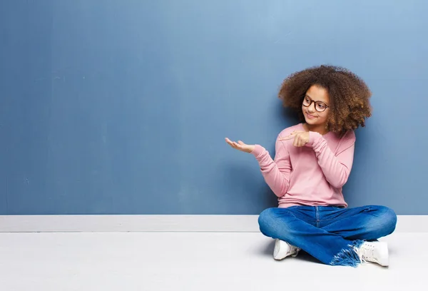 アフリカ系アメリカ人の少女は笑顔で手のひらにスペースをコピーしたり床に座っている物を見せたり宣伝したり — ストック写真