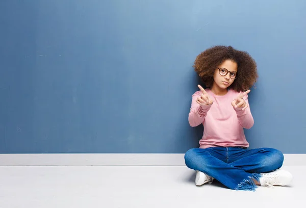 アフリカ系アメリカ人の少女は挑発的で攻撃的で卑猥な感じで真ん中の指をひっくり返し反抗的な態度で床に座り — ストック写真