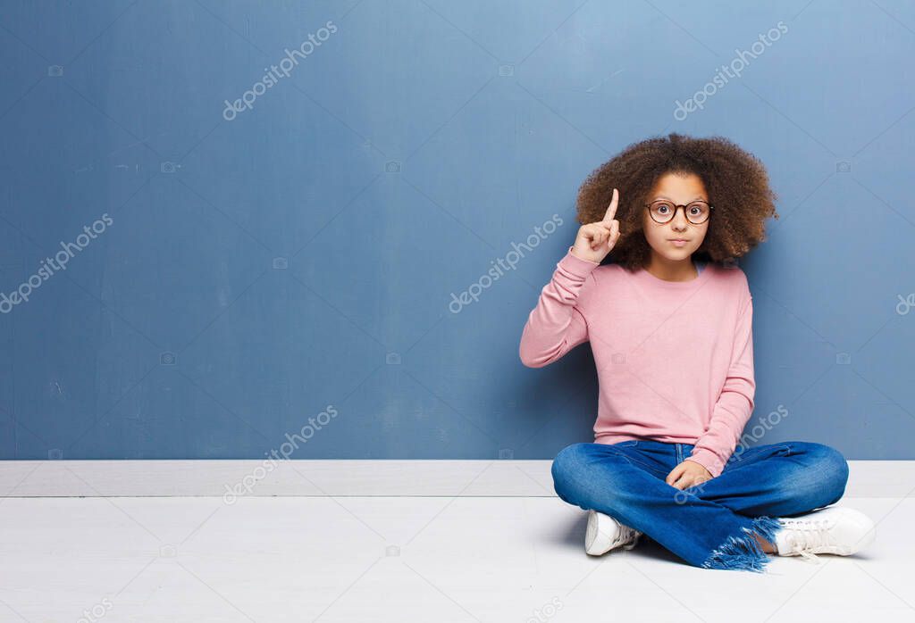 african american little girl feeling like a genius holding finger proudly up in the air after realizing a great idea, saying eureka sitting on the floor