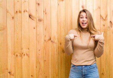 Genç sarışın kadın mutlu, şaşırmış ve gururlu hissediyor. Heyecanlı ve şaşkın bir bakışla kendini işaret ediyor.