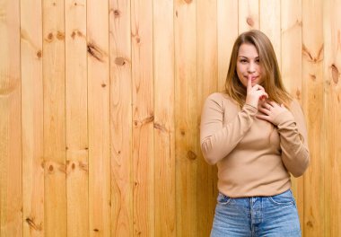 Genç sarışın kadın ciddi görünüyor ve parmaklarını dudaklarına bastırıp sessizlik ya da sessizlik talep ediyor, sır saklıyor.