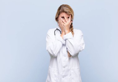 Genç ve güzel Latin bir kadın elleriyle yüzünü kapatıyor. Şaşırmış bir ifadeyle parmaklarının arasından yan tarafa bakıyor. doktor konsepti