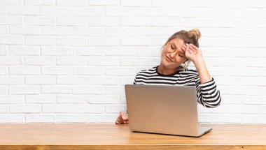 Genç ve güzel Latin kadın stresli, yorgun ve hayal kırıklığına uğramış görünüyor, alnından ter damlıyor, kendini umutsuz ve yorgun hissediyor ve dizüstü bilgisayarıyla oturuyor.