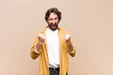 Genç, çılgın, havalı adam sinirli, sinirli bakışlar ve sıkı yumruklarla agresif bir şekilde bağırıyor, düz duvara karşı öfkeli hissediyor.