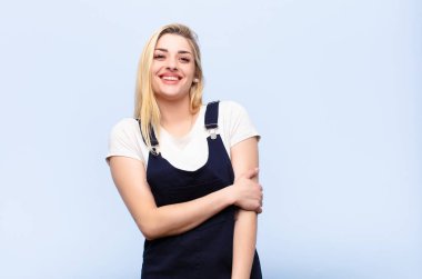 Genç, güzel, sarışın bir kadın utangaç ve neşeli bir şekilde gülüyor. Düz duvara karşı dost canlısı, olumlu ama güvensiz bir tutum sergiliyor.