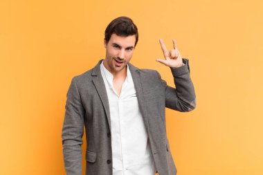 Genç yakışıklı adam kendini mutlu, eğlenceli, kendinden emin, pozitif ve asi hissediyor, elle rock ya da heavy metal işareti yapıyor.