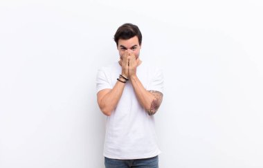 Genç yakışıklı adam mutlu, neşeli, şanslı ve şaşırmış görünüyor. İki eli de beyaz duvara dayalı.