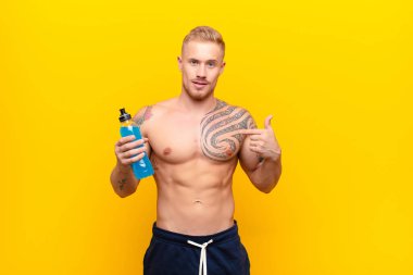 Genç, sarışın, güçlü, mutlu, şaşkın ve gururlu bir adam. Heyecanlı ve şaşkın bir bakışla enerji içeceğiyle kendini işaret ediyor.