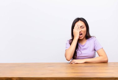 Genç Latin güzel bir kadın uykulu görünüyor, sıkılmış ve esniyor, baş ağrısı ve bir eliyle yüzünün yarısını düz duvara yapıştırıyor.