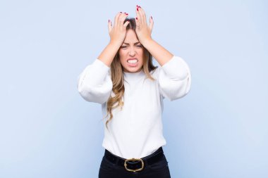 Genç ve güzel İspanyol kadın stresli ve endişeli, bunalımda ve hayal kırıklığına uğramış hissediyor, iki elini de mavi duvara doğru kaldırıyor.