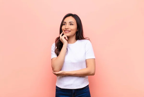 stock image young latin pretty woman smiling happily and daydreaming or doubting, looking to the side against flat wall