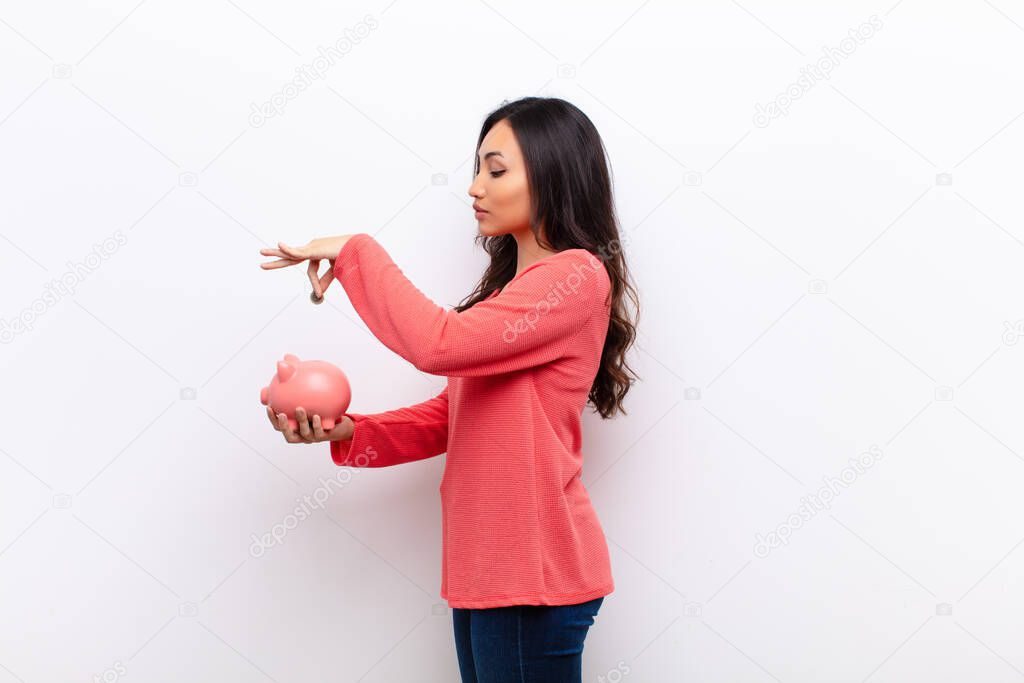 young latin pretty woman  against flat wall with a piggy bank