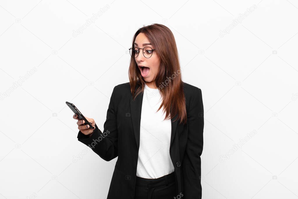 young businesswoman looking very shocked or surprised, staring with open mouth saying wow and holding a mobile telephone