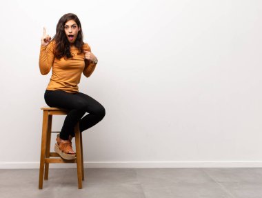 Genç ve güzel bir kadın öfkeyle bağırıyor, agresif bir şekilde bağırıyor, stresli ve sinirli bir şekilde odada oturuyor.