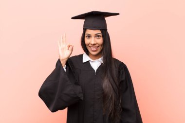 Genç Latin kız öğrenci kendini mutlu, rahat ve tatmin olmuş hissediyor. Onayını iyi bir hareketle gösteriyor. Gülümsüyor.