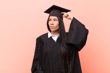 Genç Latin kız öğrenci şaşkın ve kafası karışmış hissediyor, başını kaşıyor ve yan tarafa bakıyor.