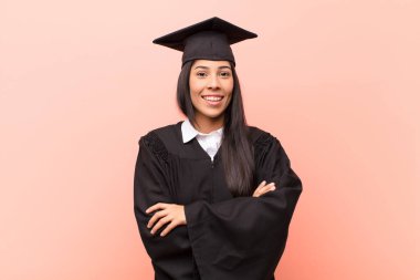 Kollarını kavuşturup gülümseyen mutlu, gururlu ve tatmin olmuş genç bir Latin kız öğrenci.