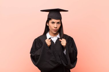 Genç Latin kız öğrenci kendinden emin, sinirli, güçlü ve agresif görünüyor. Yumrukları boks pozisyonunda dövüşmeye hazır.