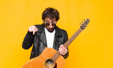 Genç müzisyen şok olmuş, ağzı açık ve hayret içinde, gitar, rock 'n roll konseptiyle inançsızlık ve şaşkınlığa doğru bakıyor ve işaret ediyor.