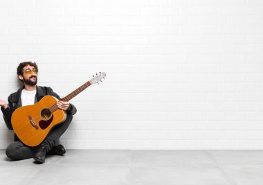 Genç müzisyen şaşkın ve şaşkın hissediyor, şüpheci, farklı seçenekleri tartıyor ya da seçiyor gitar, rock 'n roll konseptiyle komik bir ifadeyle