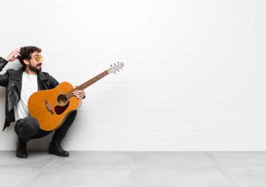 Genç müzisyen şaşkın ve kafası karışmış hissediyor, kafasını kaşıyor ve gitar, rock 'n roll konseptiyle yan tarafa bakıyor.
