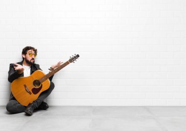 Genç müzisyen şaşkın, kafası karışmış ve stresli görünüyor, farklı seçenekler arasında merak ediyor, gitar, rock and roll konsepti konusunda kararsız.
