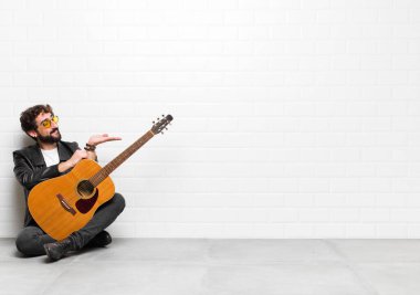 Genç müzisyen kendini mutlu hissediyor ve gülümsüyor. Elinde gitar, rock 'n roll konseptiyle bir objeye ya da konsepte bakıyor.